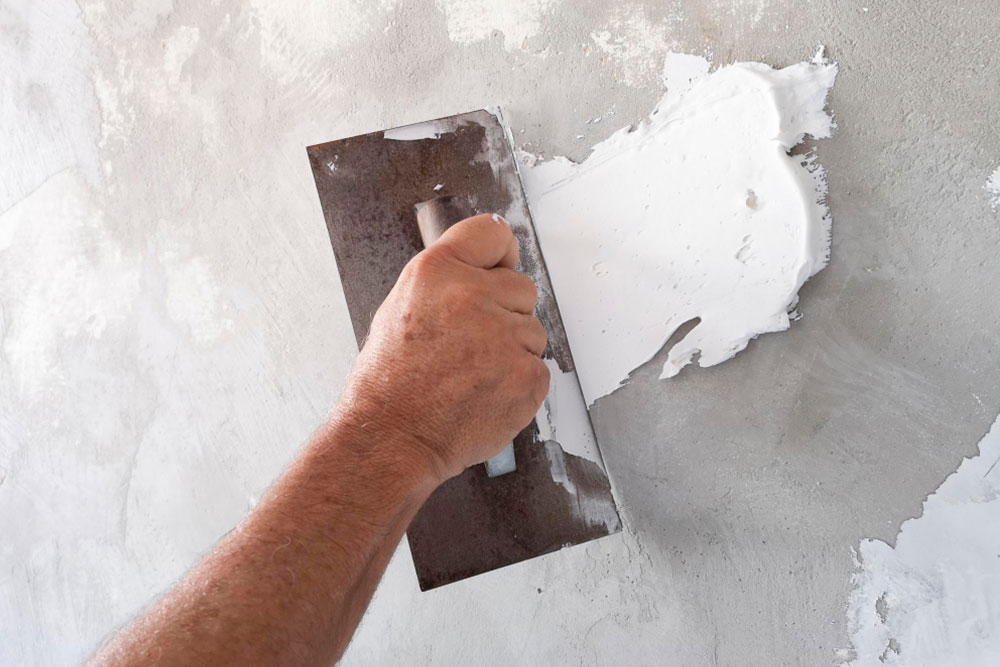 Eine Hand, die einen Spachtel hält und eine Wand mit Spachtelmasse verputzt