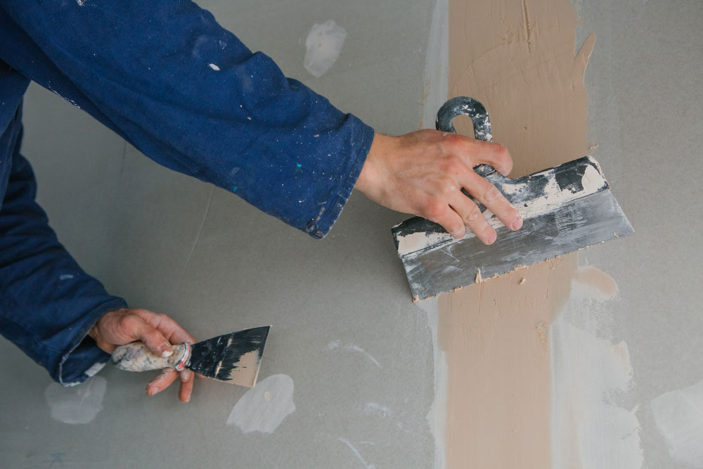 Zwei Hände mit Spachteln an einer Trockenbauwand
